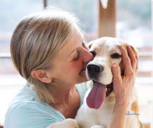 A woman gently holding and kissing a happy dog, representing a calm and loving connection with animals.