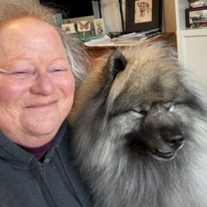 Cat Malkin smiling beside her fluffy Keeshond dog, Yogi Bear, sharing a calm and peaceful moment together indoors.